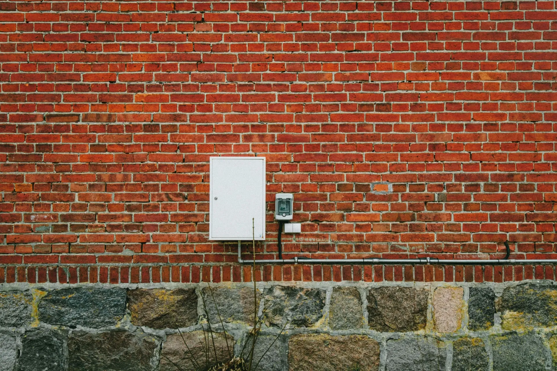 Electricity meter box mounted on a red brick wall above a stone base
