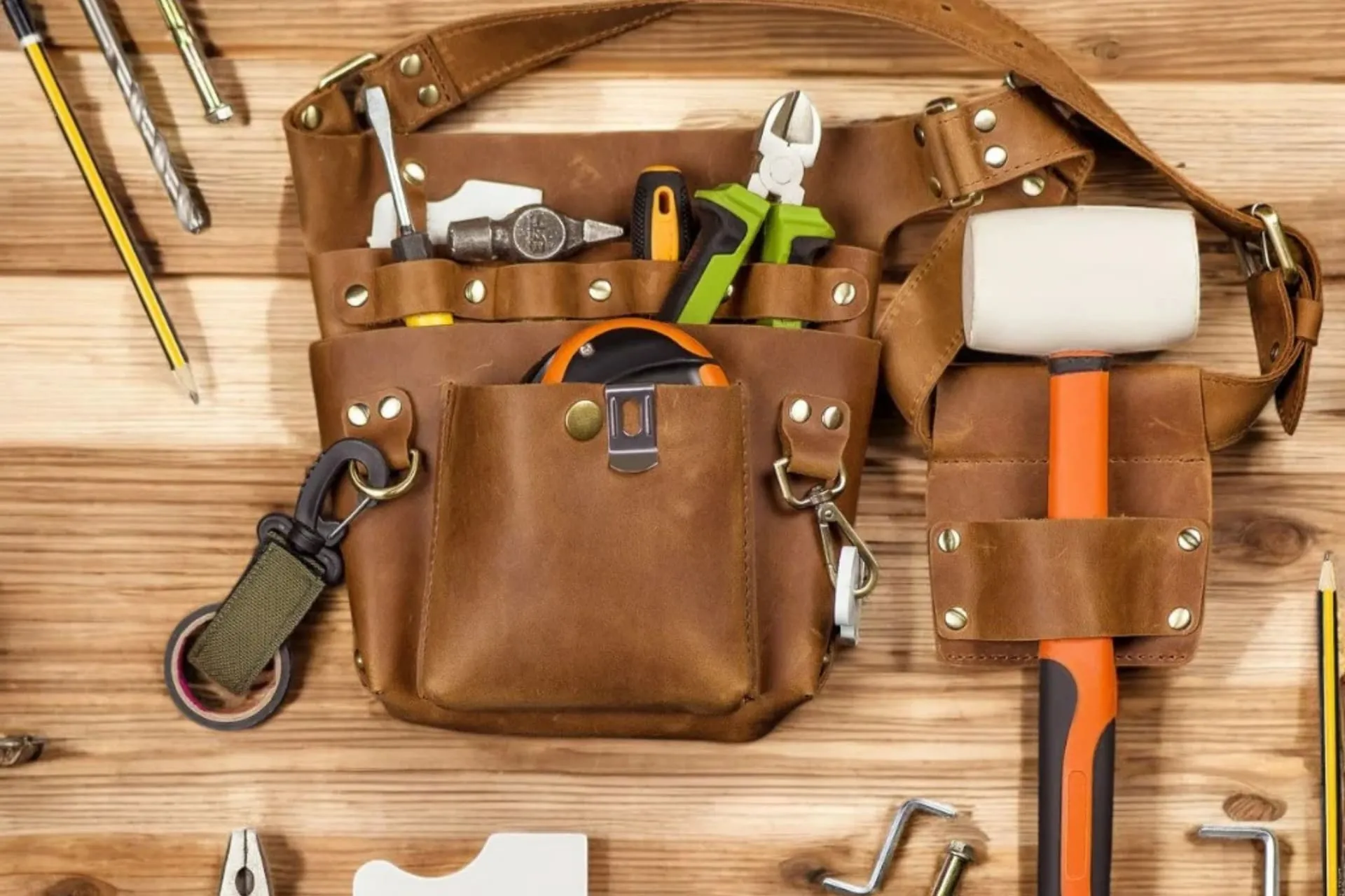 Leather tradie tool belt loaded with pliers, screwdrivers and a hammer on a workbench