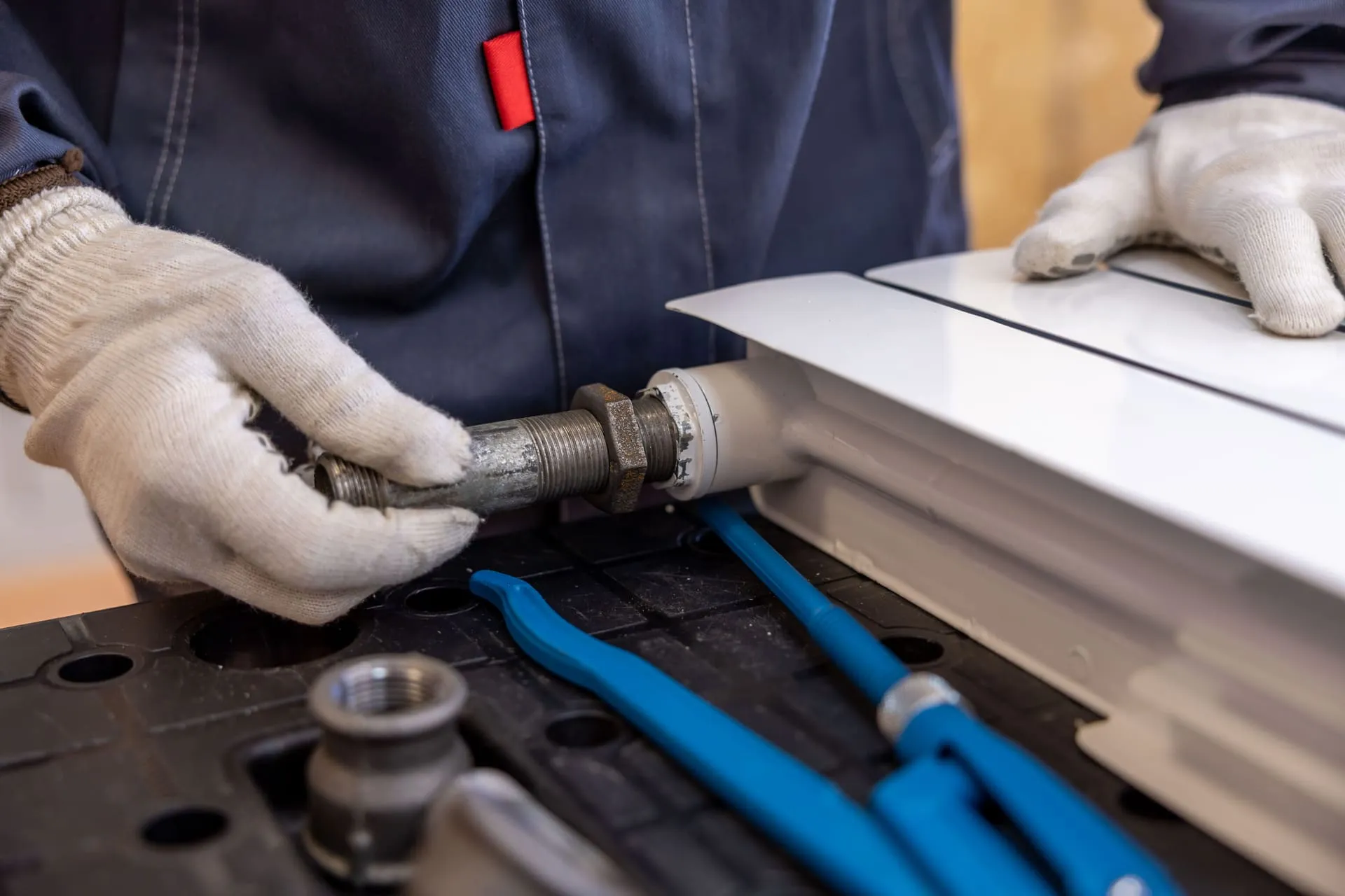 Gloved plumber tightening a threaded pipe fitting into a radiator connection