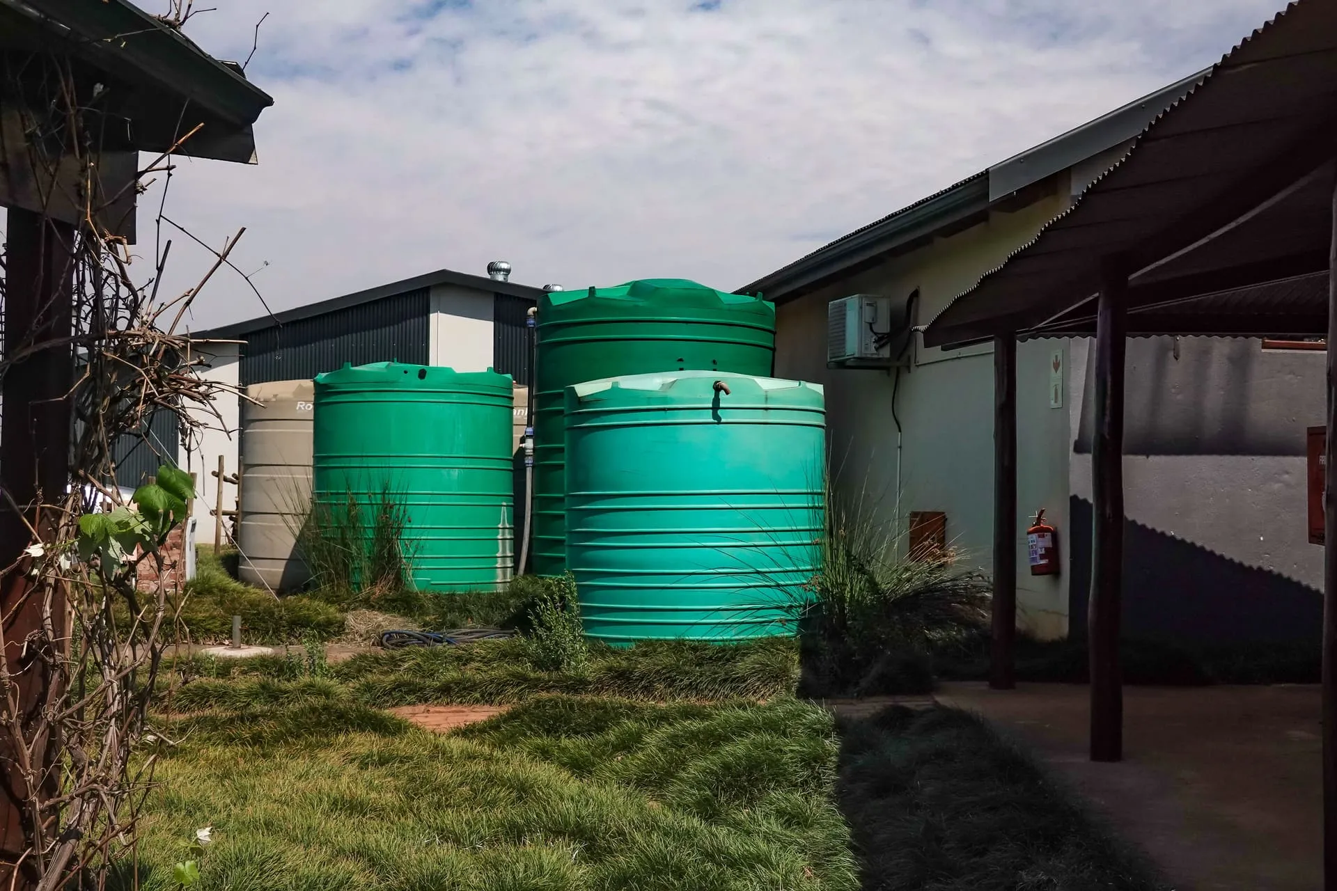 Green poly water tanks standing beside a building in a grassy yard