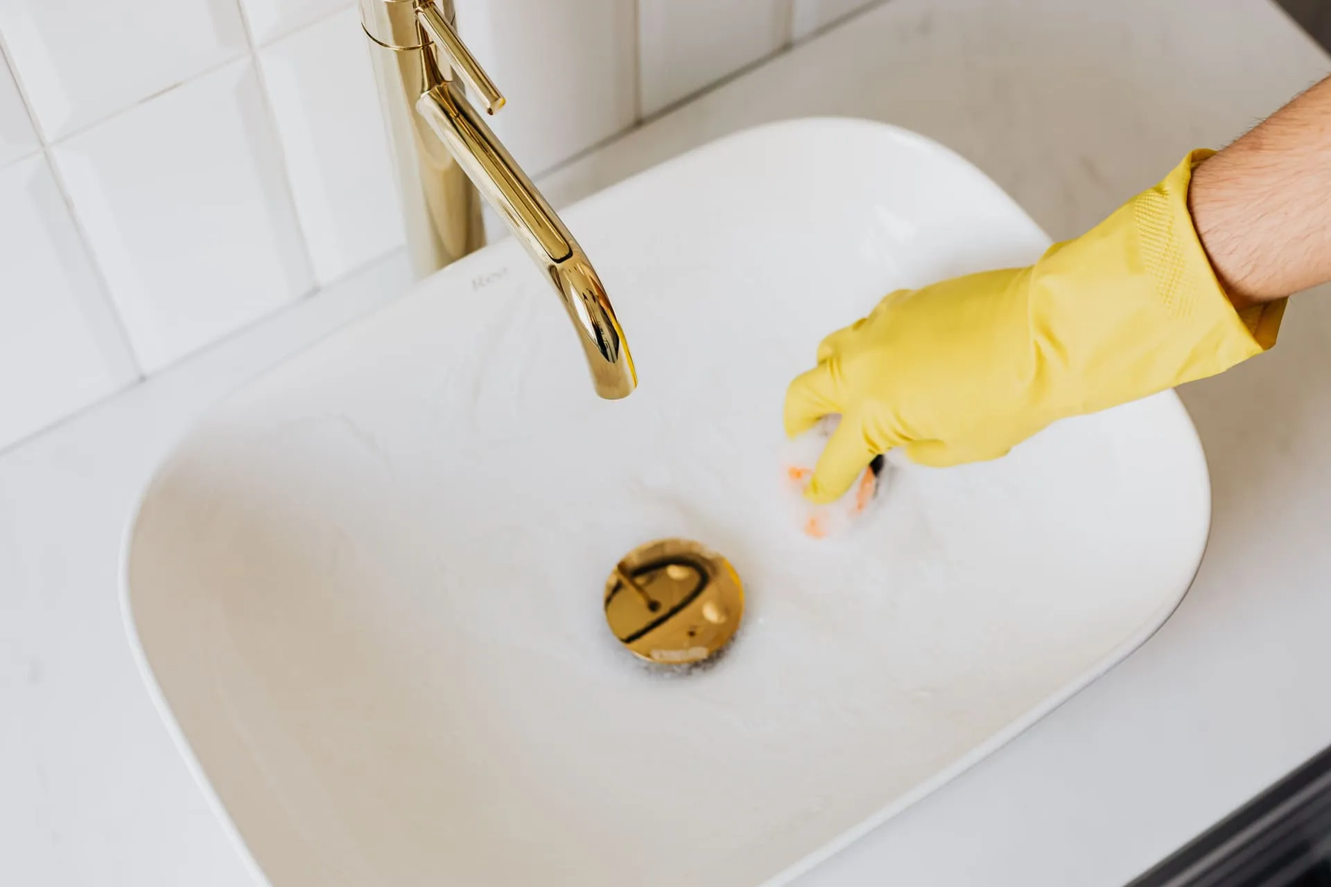 Gloved hand clearing a bathroom basin plug, the best way to unblock a drain