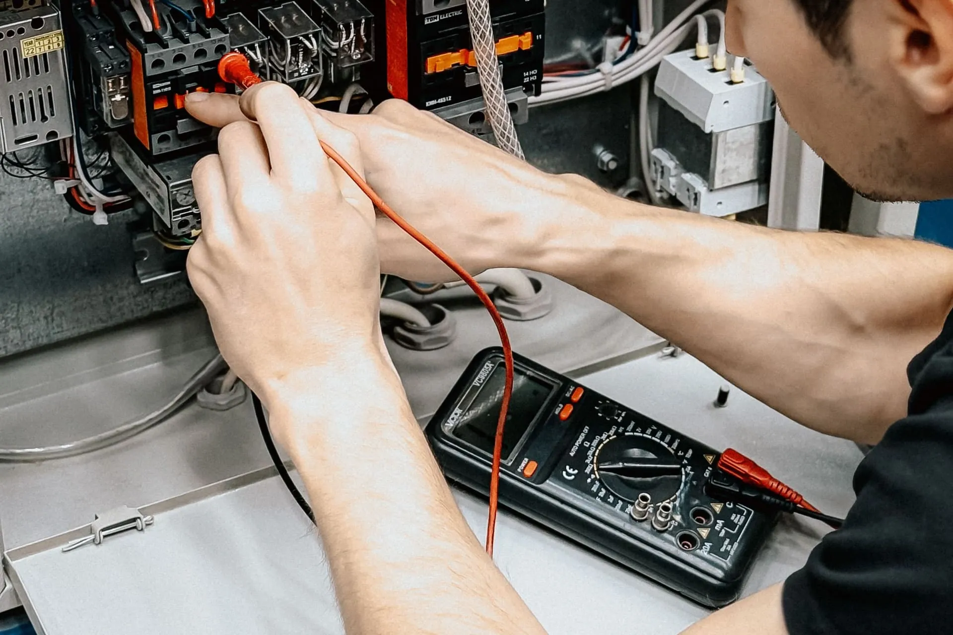 Electrician testing a switchboard with a multimeter before issuing an electrical certificate of compliance