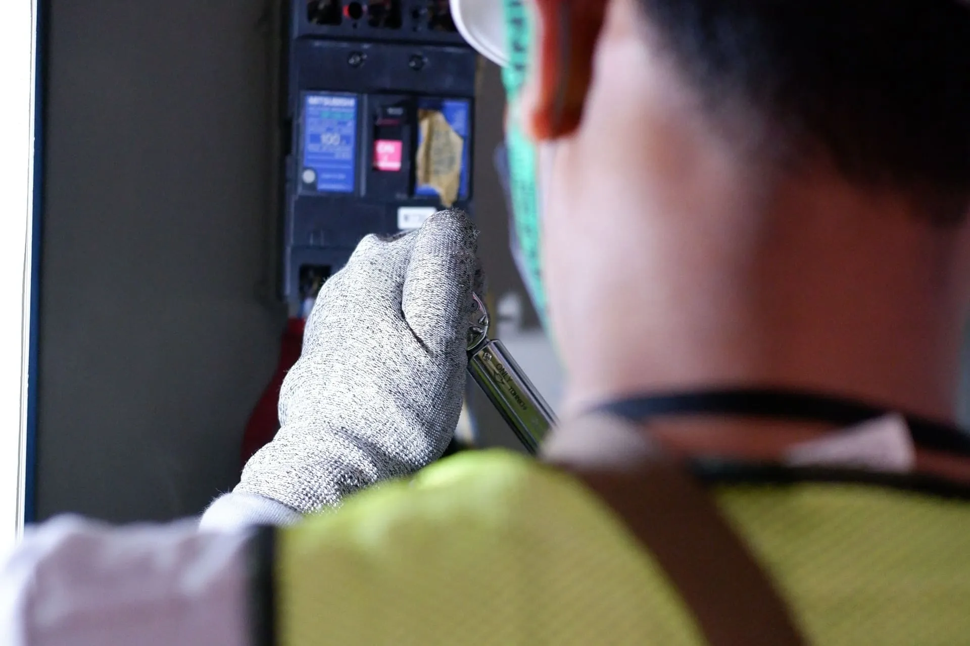Emergency electrician in hi-vis and gloves working on a circuit breaker in a switchboard