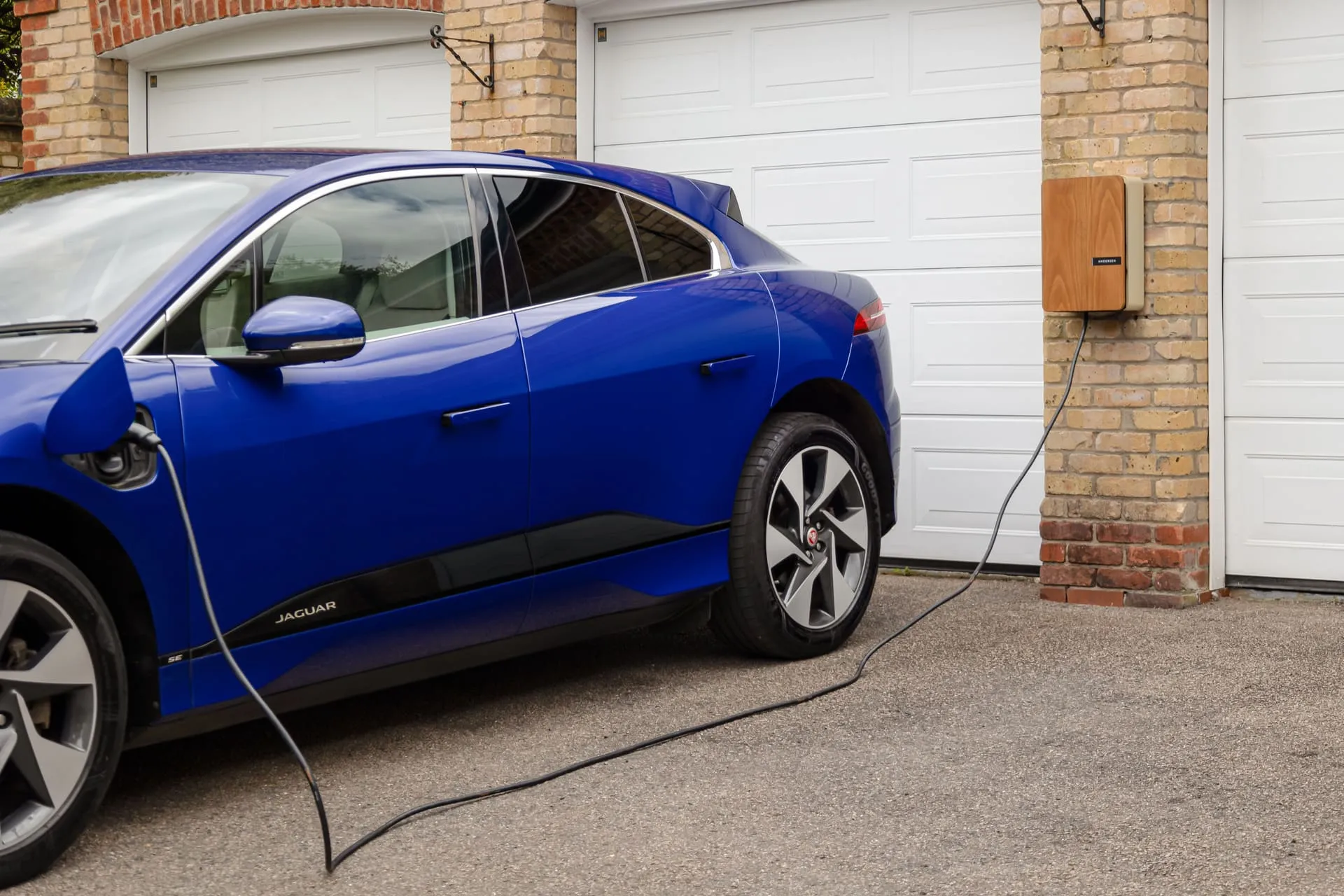 Electric car plugged into a wall-mounted home EV charger beside a garage door