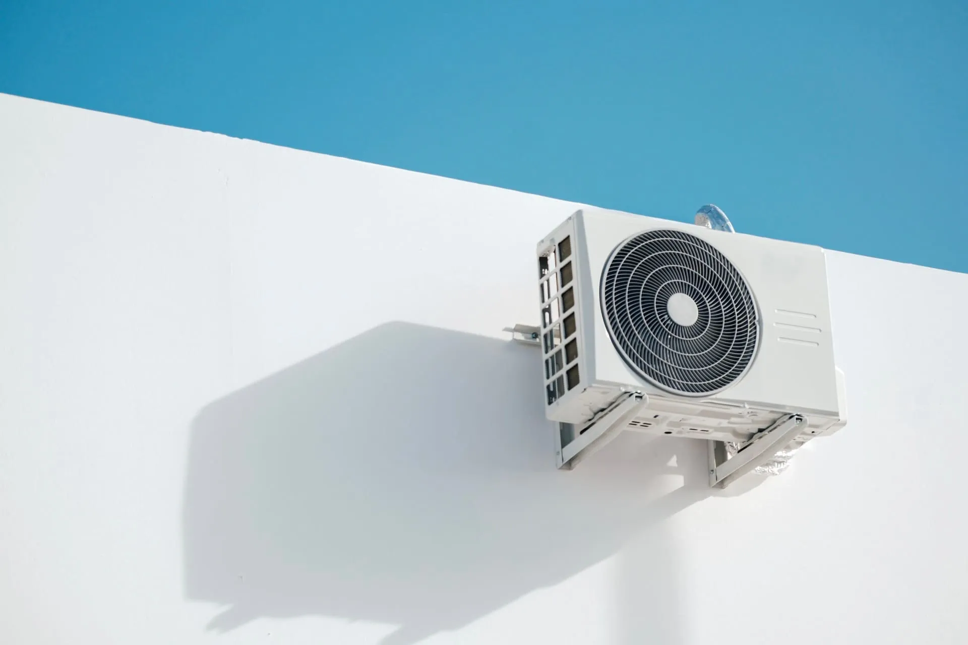 Outdoor heat pump compressor unit mounted on a white wall, as used in a heat pump hot water system