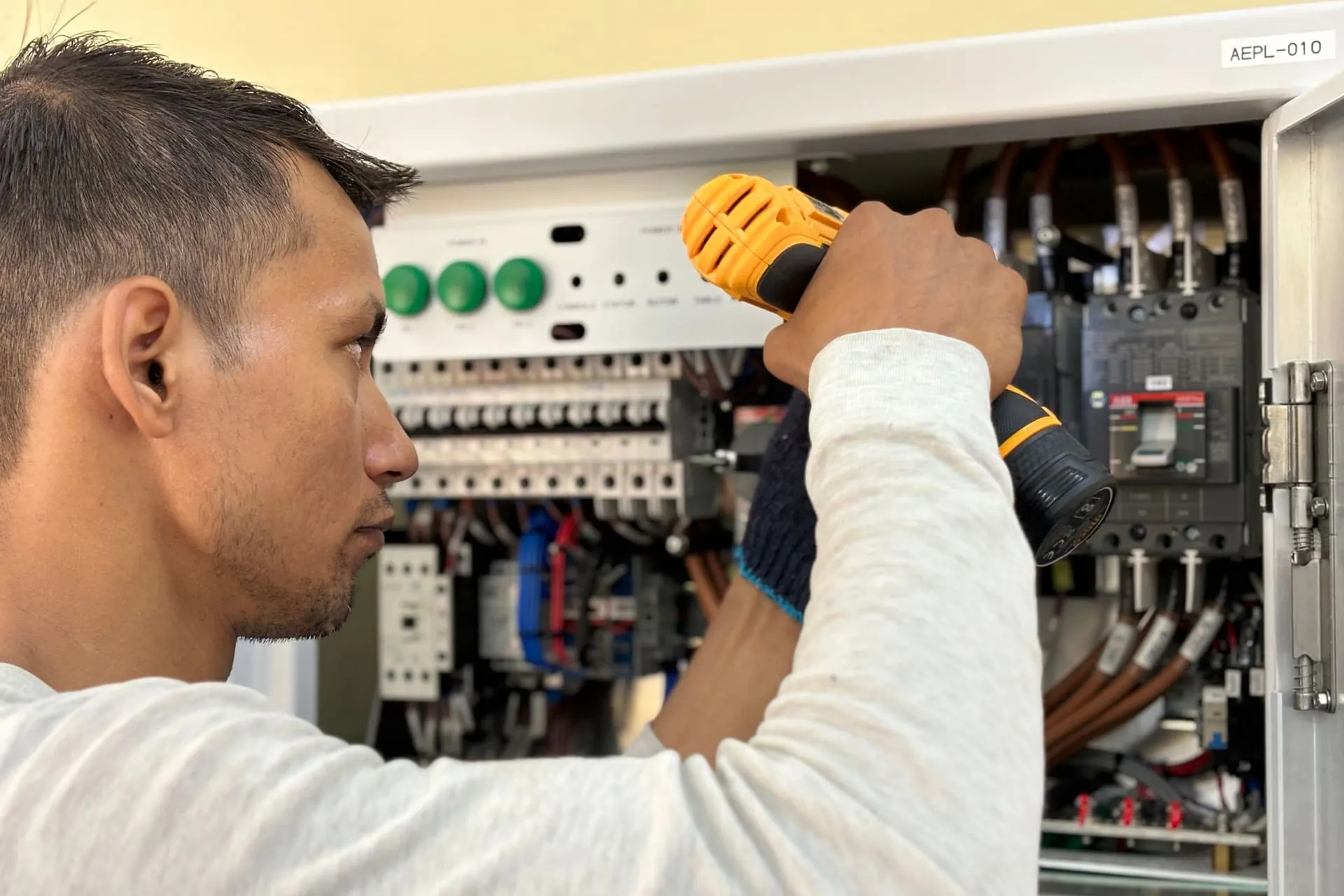 Electrician in work gloves fitting circuit breakers inside an open electrical switchboard