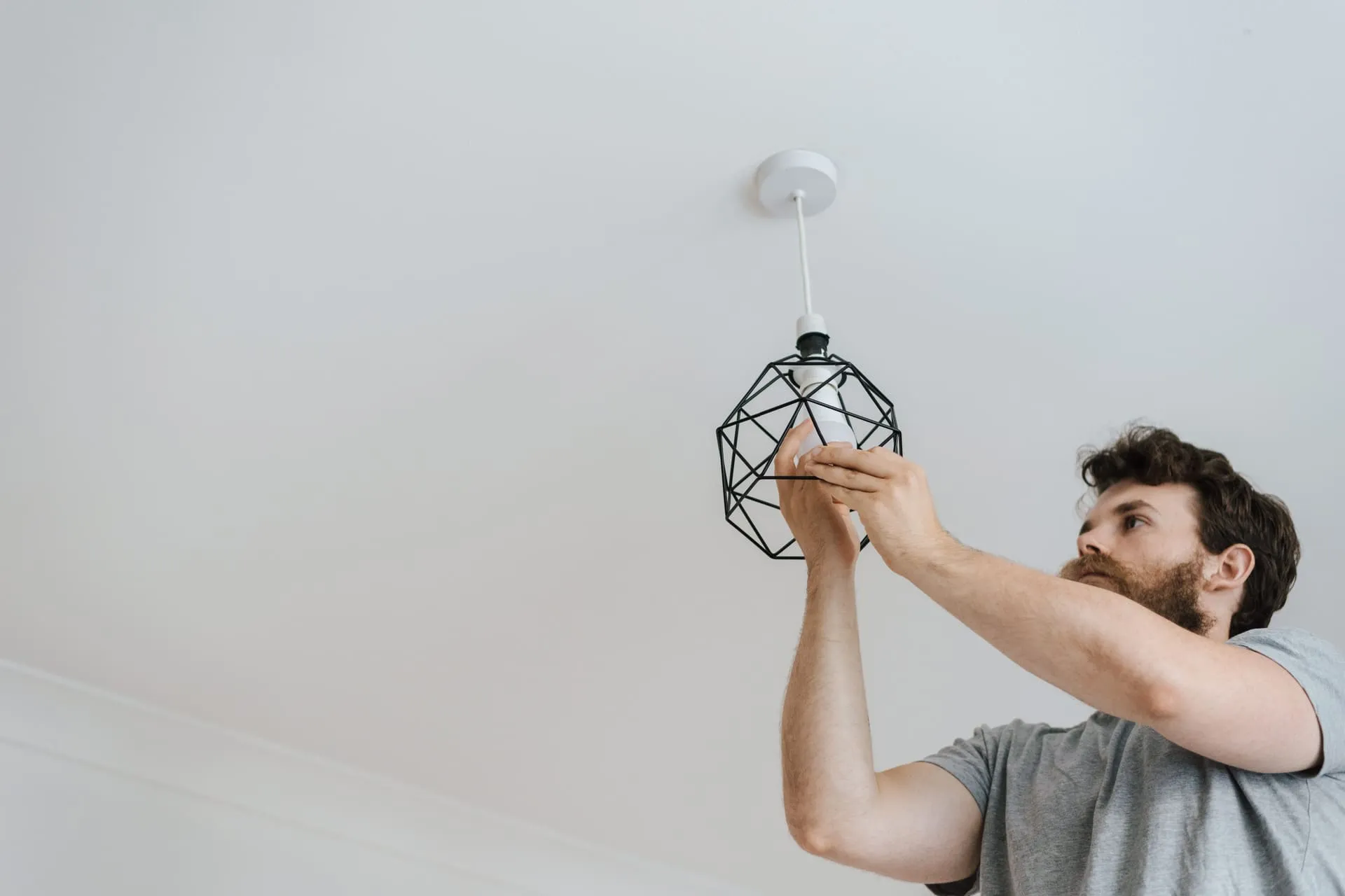 Electrician fitting a black cage pendant light to a white ceiling
