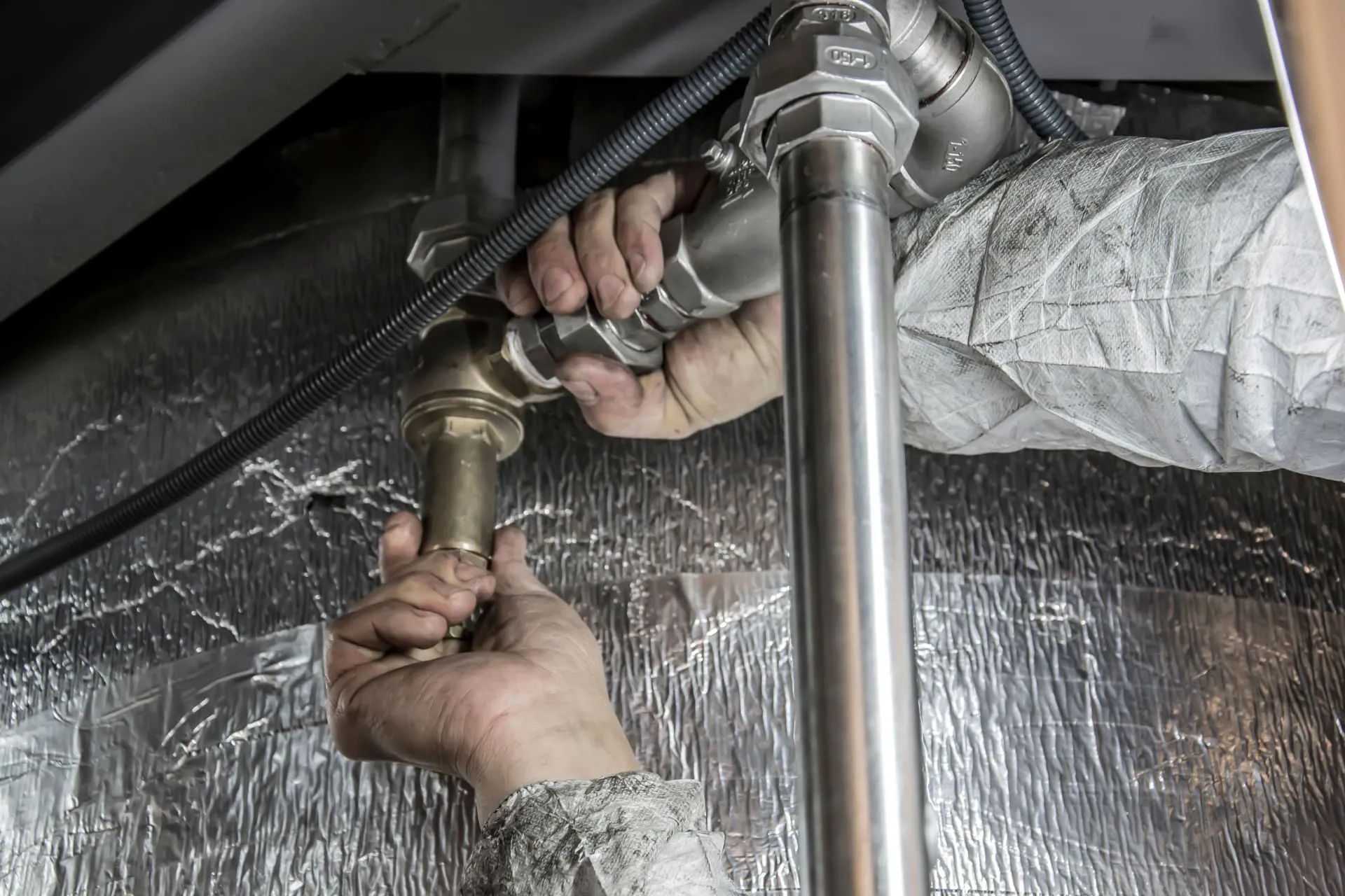 Plumber tightening a threaded steel pipe joint beside insulated pipework
