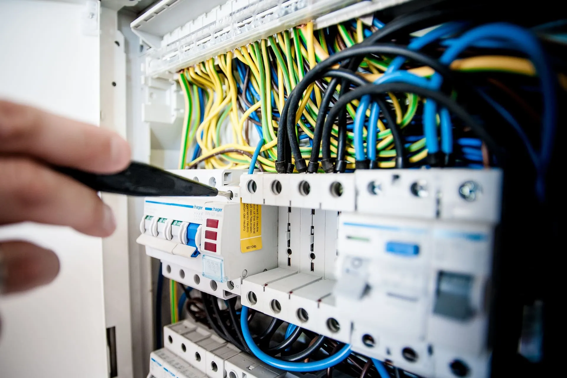 Electrician's screwdriver at a row of safety switches and circuit breakers in a switchboard