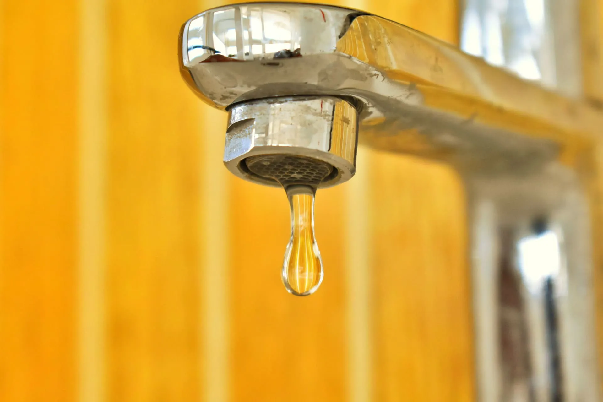 Water drop falling from a chrome mixer tap, a common leaking tap repair