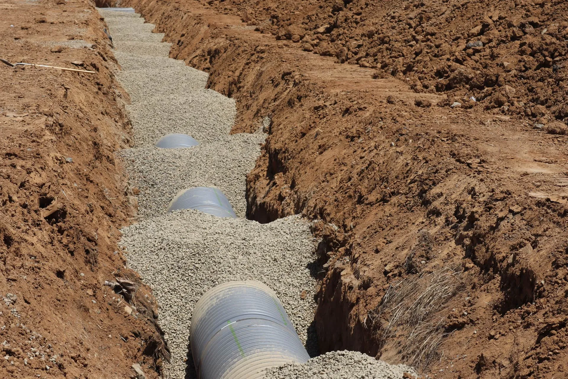 Trench with exposed drainage pipe in gravel, where tree roots in pipes cause blockages